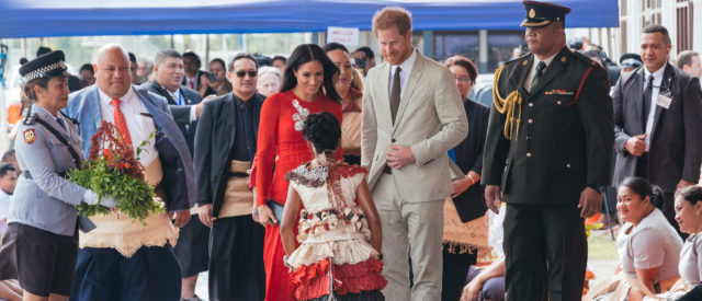 In this photo, the Duke and Duchess arrive in Tonga during their Pacific tour in 2018. A young local girl gifts the Duchess with a bouquet of flowers while the welcoming entourage gather behind for this official welcome to this island nation
